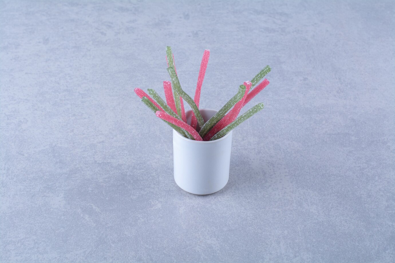 A cup with sugary jelly fruit sticks candies on gray background 