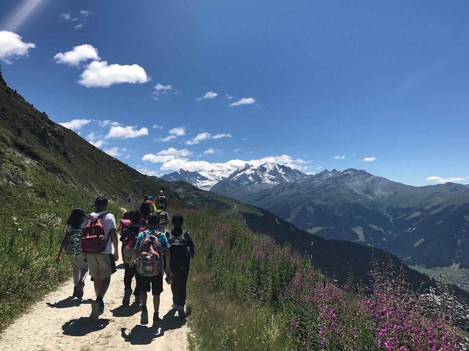 children hiking in the beautiful trails of Verbier during their 2024 summer camp at Les Elfes International. Beautiful scenery with snowy mountains and pink flowers